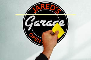 Hand using yellow squeegee to apply a circular wall decal that says Jared's Garage.