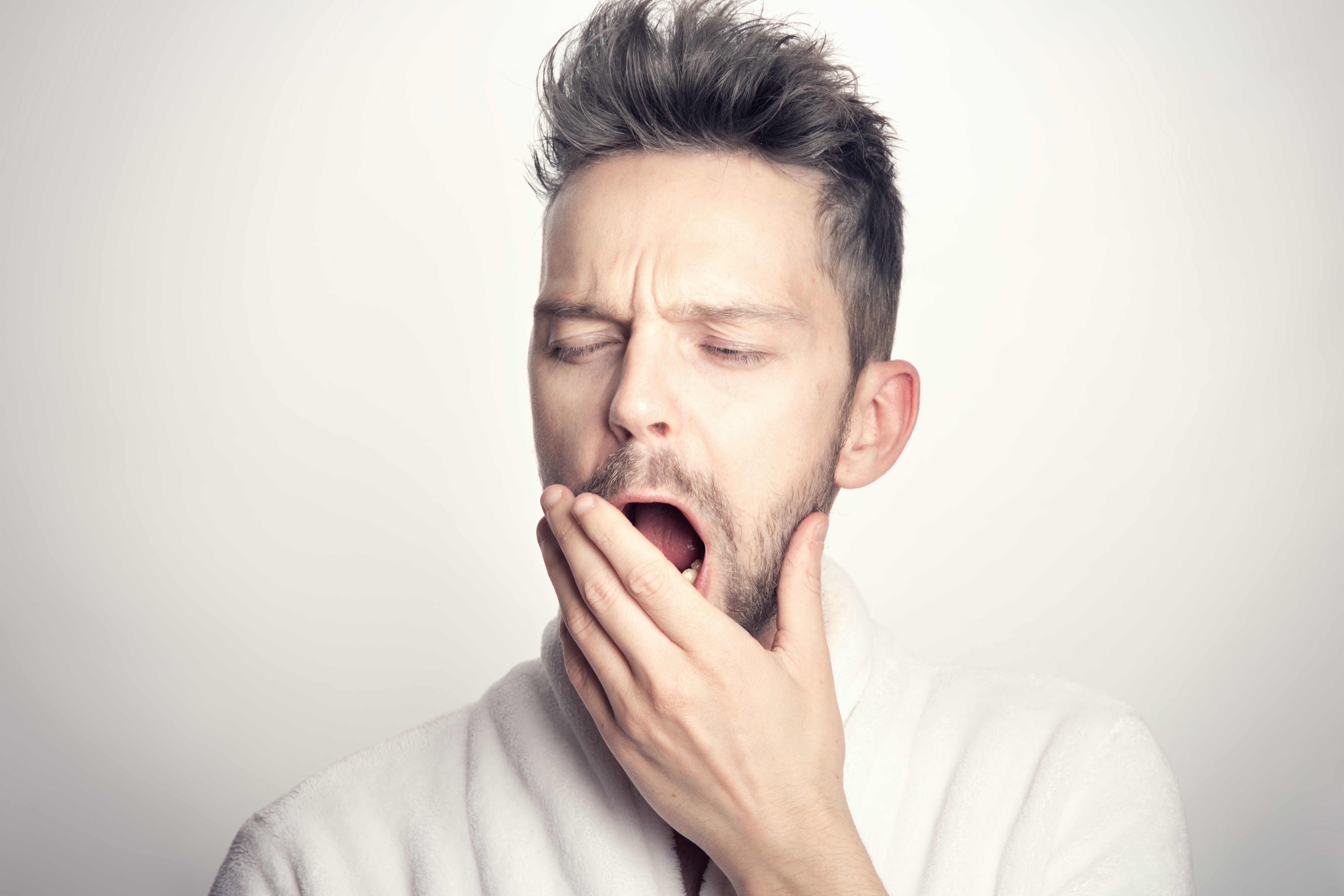 Short-haired brunette young man in gray t-shirt yawning