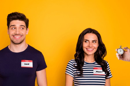 a man and woman wearing name tags for speed dating event with a stop watch timing them