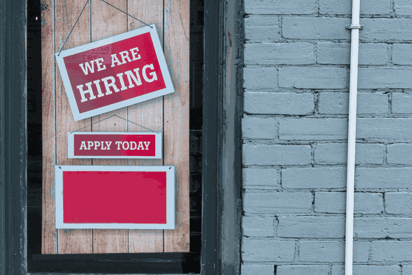 hanging red we are hiring sign in doorway connected to a brick builing